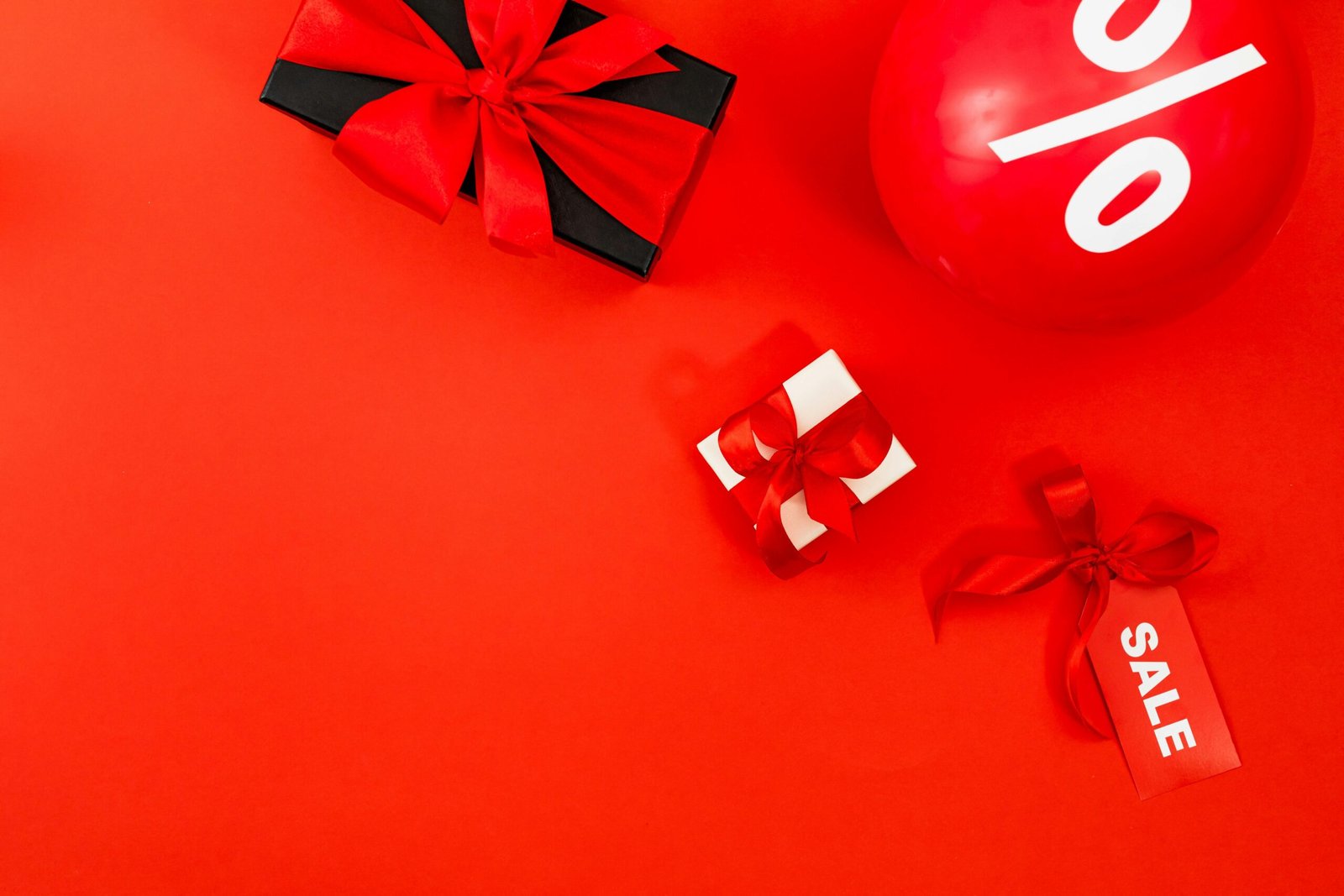 Bright red sale display with gifts and percentage balloon on red background.